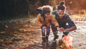 Man teaching boy how to fish with fishing net in mountain stream at sunset